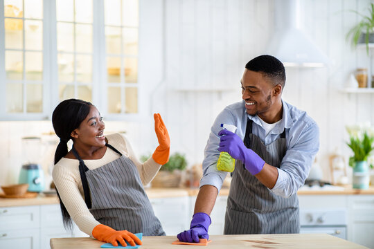 Black Guy Being Silly During House Cleanup, Pretending To Spray His Girlfriend From Detergent Bottle At Kitchen