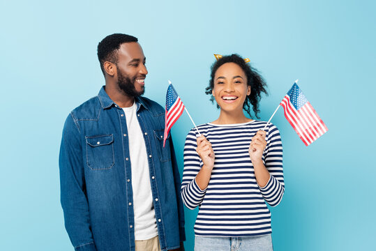 smiling african american man looking at happy wife holding small flags of usa on blue
