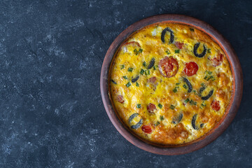 Frittata with egg, pepper, onion, olives, tomato and cheese on table. Italian egg omelette