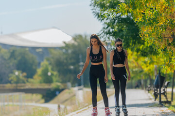 Two beautiful sportswomen roller skating in the park on a sunny day