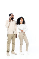 happy african american couple talking on mobile phones and looking away on white