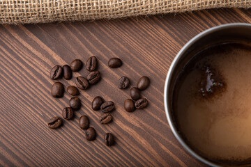 Metallic old-school cup with black coffee made in it placed on a wooden table with coffee beans