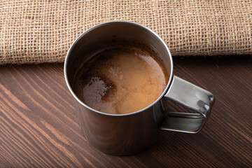 Metallic old-school cup with black coffee made in it placed on a wooden table
