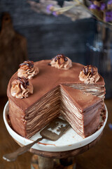 Chocolate crepe cake decorated with cream, chocolate and nuts. Wooden background. In the background is a gray wooden background. Chocolate, coffee, purple flowers.  Easter. Side view.