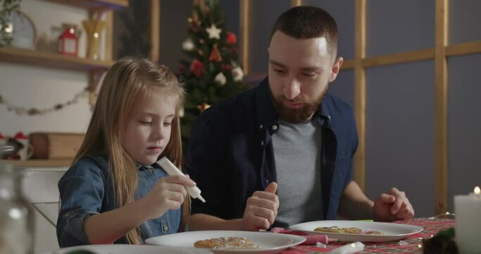 the girl helps her beloved dad to paint gingerbread