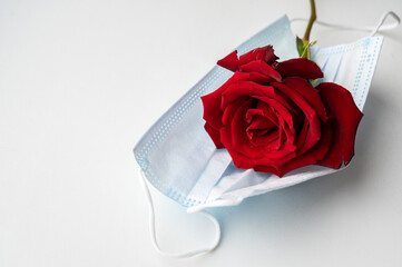 Beautiful red rose on a medical mask, on a white background. A safe holiday during an epidemic. Protection against coronavirus.