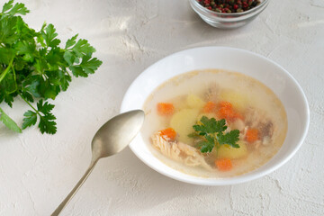 Clear fish soup with pieces of vegetables and salmon with spices in a white bowl on a white plate. Healthy nutrition concept. Top view. Horizontal orientation.