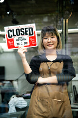 Asian female hairdesser closed sign board on glass door in modern salon.