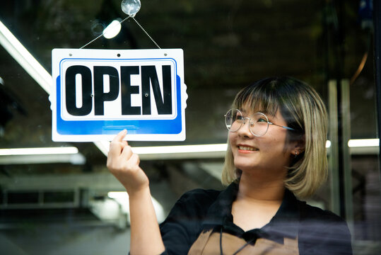 Asian Female Hairdesser Of Salon Shop Turning Round Open Sign On A Door.