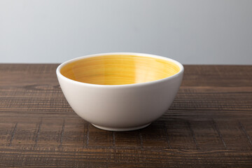 Empty white bowl with hand painted yellow inside. Isolated on wooden background