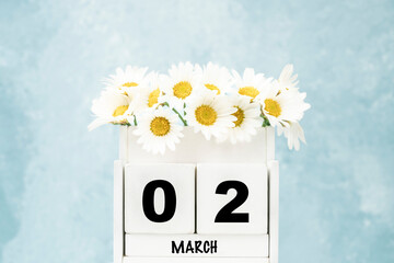 cube calendar for March with daisy flowers over blue with copy space