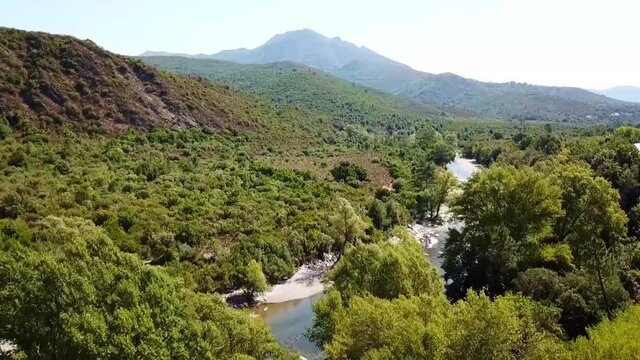 Drone takes off over a river. The mountains of Corsica and the evergreen scrub forest - macchia can be seen. France