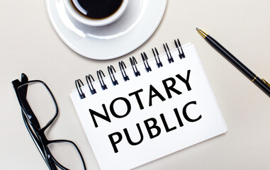 Glasses, a white cup of coffee, a white notebook with the words NOTARY PUBLIC and a ballpoint pen lie on a light background. Flat lay. View from above.