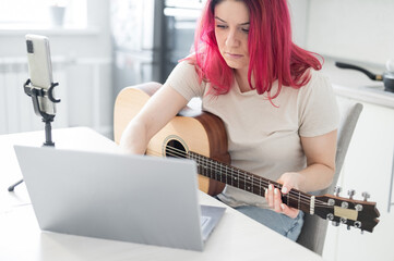 A woman sits in the kitchen during a remote acoustic guitar lesson. A girl learns to play the...