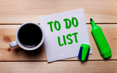 On a wooden table, a cup of coffee, a green marker and a napkin with the text TO DO LIST