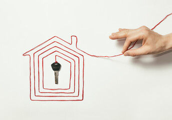 The human hand pulls on the thread laid out in the shape of a house with a key at the end.