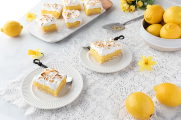Lemon meringue squares on serving plates with more on a marble platter in behind. 