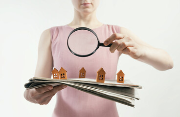 The woman with magnifier holds a newspaper with paper houses in front of yourself. Concept of real...