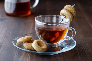 Close up of a glass cup of tea served with mini sugar and cinnamon donuts, ready for eating.