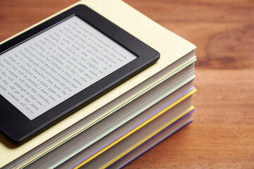 Electronic reader with a text on the screen on a stack of books on a wooden desk