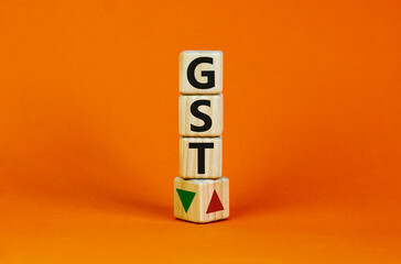 GST, goods and services tax symbol. Wooden cubes with up and down icon. Word 'GST'. Beautiful orange background. Copy space. Business and growth of GST, goods and services tax concept.