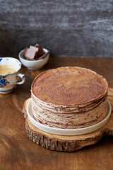 Chocolate crepe cake decorated with cream, chocolate and nuts. Wooden background. In the background is a gray wooden background. Chocolate, coffee, purple flowers. Side view.
