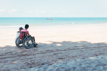 Fototapeta na wymiar Asian special child on wheelchair is fun, playing and exercise activity on sea beach at summer, Lifestyle of disability child, Life in the education age, Happy disabled kid in travel concept.