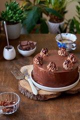 Chocolate cake decorated with cream, chocolate and nuts. Wooden background. In the background is a gray wooden background. Chocolate, coffee, purple flowers. Side view.