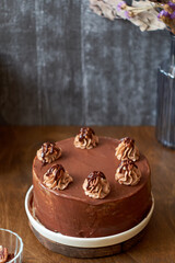 Chocolate cake decorated with cream, chocolate and nuts. Wooden background. In the background is a gray wooden background. Chocolate, coffee, purple flowers. Side view.