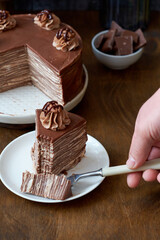 Chocolate crepe cake decorated with cream, chocolate and nuts. Wooden background. In the background is a gray wooden background. Chocolate, coffee, purple flowers. Side view.