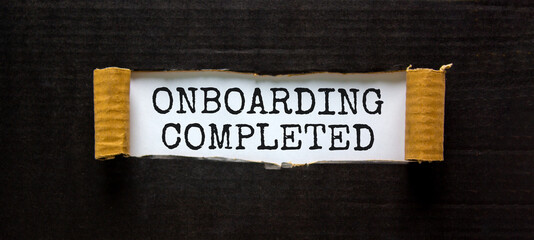 Onboarding completed symbol. Words 'Onboarding completed' appearing behind torn black paper. Beautiful black background. Business, onboarding completed concept, copy space.