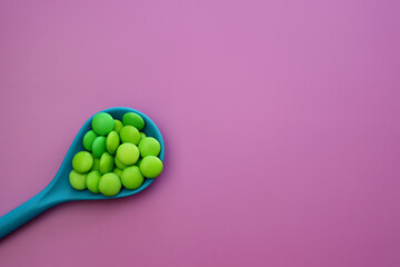 Green sweet drops in a blue spoon on a light pink background
