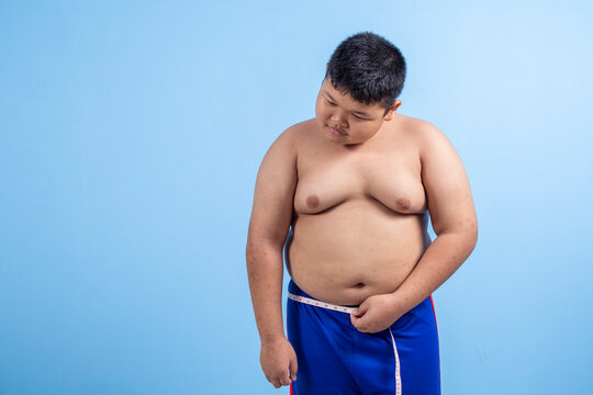 Fat boy with sad face measuring his waist on sky blue background in studio. Asian boy has bad skin and overweight.