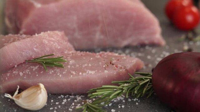 Close up of fresh pork is sprinkled with pepper, spices and seasonings on background of vegetables. Food concept, cooking meat steak, loin, carbonate.
