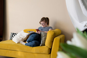 Portrait of smiling teenager girl with Down syndrome using smartphone while sitting on sofa in...