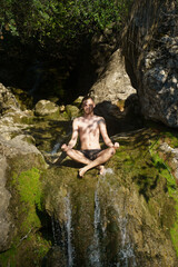 Blond Caucasian man meditating without shirt on top of a waterfall. Palma de Mallorca, Spain