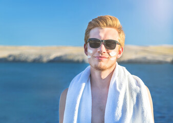 Attractive man with protective sun cream (solar cream, sunscreen ) on the face for care of his body. Young handsome caucasian male model with red hair in sunglasses. Healthy skin.