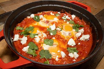 A delicious pot of Shakshuka with avocado and harissa eggs boiling in a large red cook pot