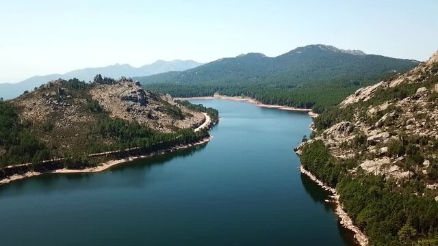 Drone flies backwards over a reservoir. You can see the mountains of Corsica and the bush forest macchia. France