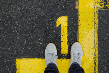 Men with grey sneker and jeans stand on the number 1, sign on the asphalt, yellow painted number...