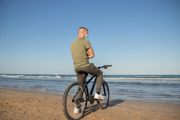 Fototapeta premium Boy with green shirt and mask arriving at his destination after a bike ride to rest on the beach
