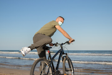 Boy with green shirt and mask arriving at his destination after a bike ride to rest on the beach