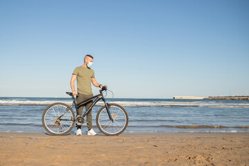 Boy with green shirt and mask arriving at his destination after a bike ride to rest on the beach