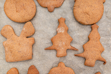 Baked gingerbread cookies in various shapes without decorations, lying on baking paper, top view.
