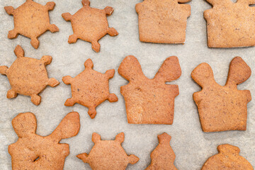 Baked gingerbread cookies in various shapes without decorations, lying on baking paper, top view.