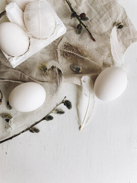 Natural easter eggs, feathers, pussy willow branches on rustic cloth on white aged table. Flat lay