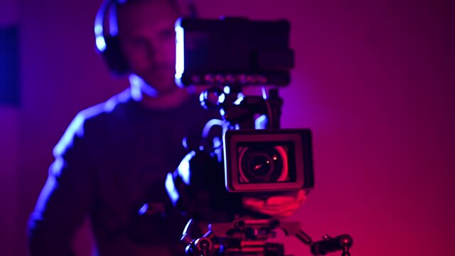 Video Production Stage Dark Red and Blue Illuminated and Film Making Professional Digital Camera Operator at Work. Caucasian Men in His 40s.