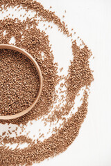 Buckwheat kernels in wooden bowl is randomly scattered on a white background. Top view. Copy, empty space for text