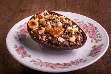 Mini stuffed chocolate with hazelnut easter egg on a white plate with flower design on a wooden table.
