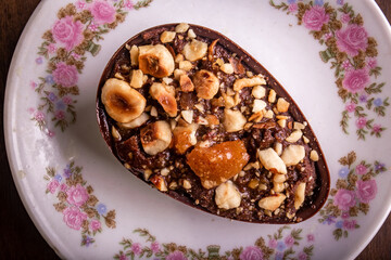 Top view of mini stuffed chocolate with hazelnut easter egg on a white plate with flower design on a wooden table.